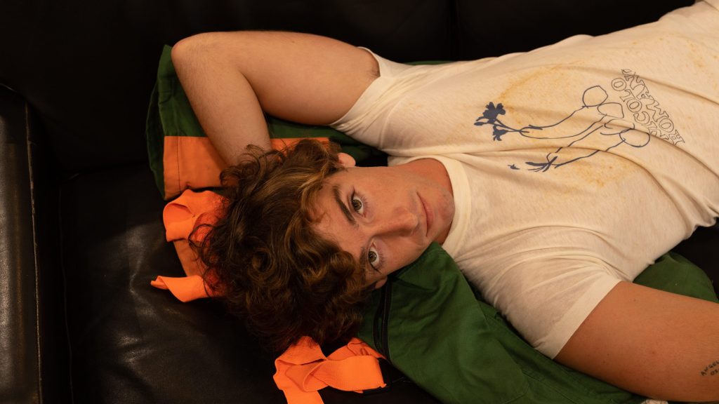 Guitarricadelafuente tumbado en un sofá con mirada directa, vestido con camiseta blanca durante la era Spanish Leather